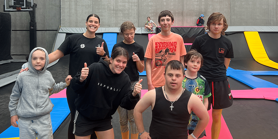 A group of young people standing together smiling on trampolines at an activity centre